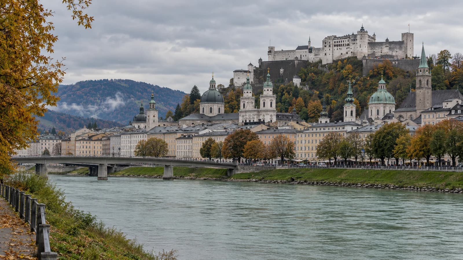 KI-generiertes redaktionelles Motiv der Salzburger Altstadt an der Salzach mit der Festung Hohensalzburg über herbstlichen Dächern.